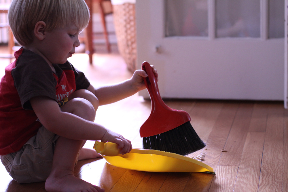 Little boy cleaning the floor holding dust brush